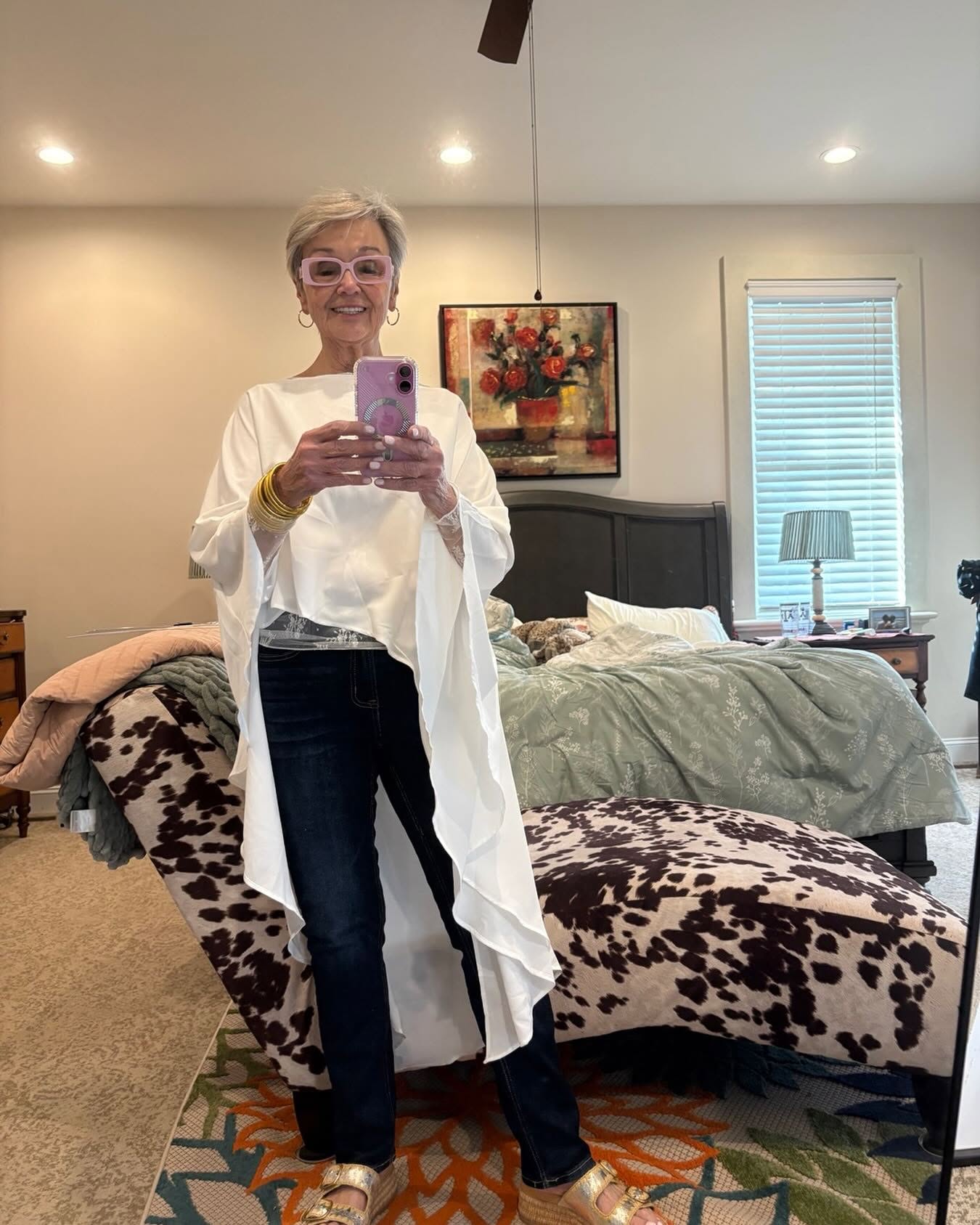Mindy in a flowy white top and dark jeans, mirror selfie with gold bangles